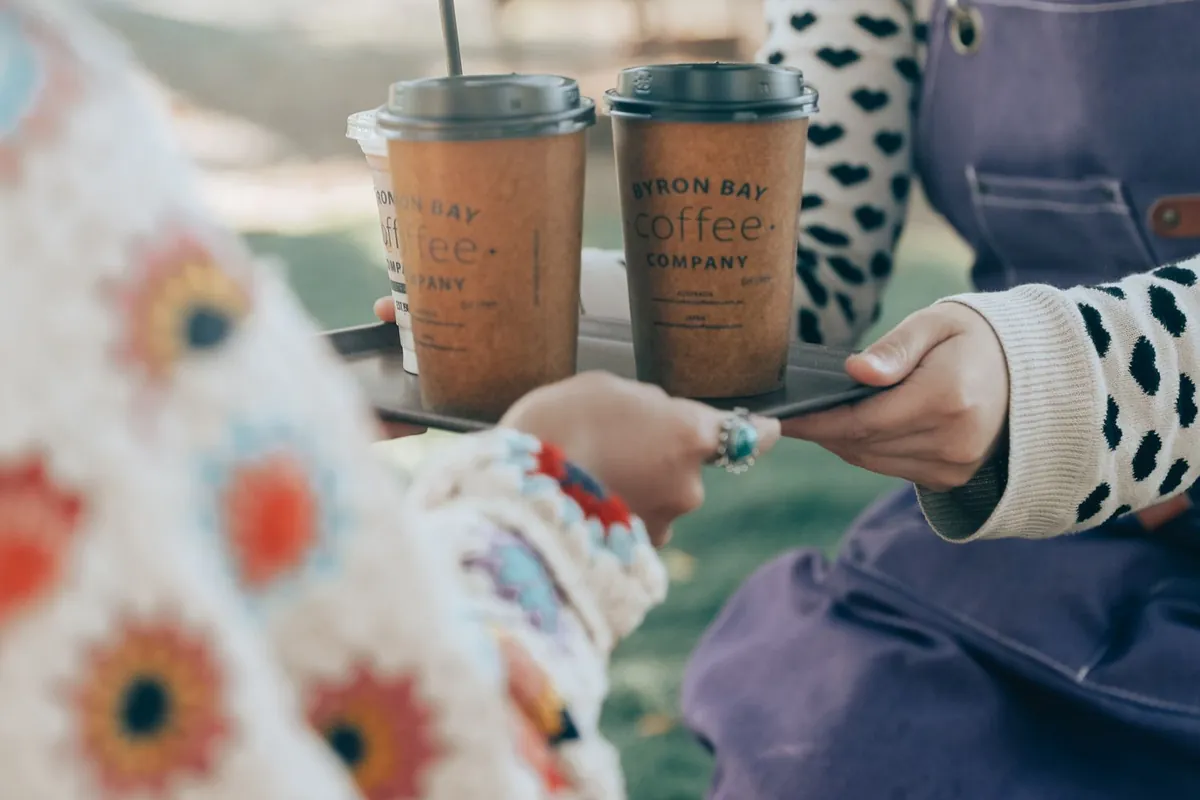 Byron Bay Coffee のテイクアウトカップを受け取る手元